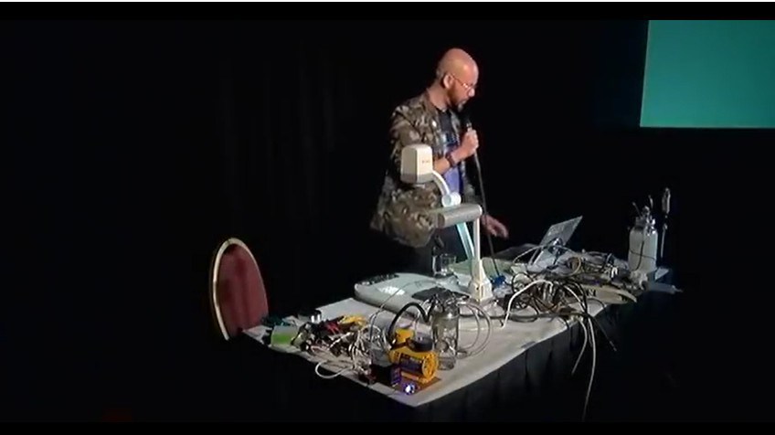 Dr. Michael Laufer with the 3D printed chemical reactor kit at the HOPE conference. Image via Michael Laufer/Youtube.